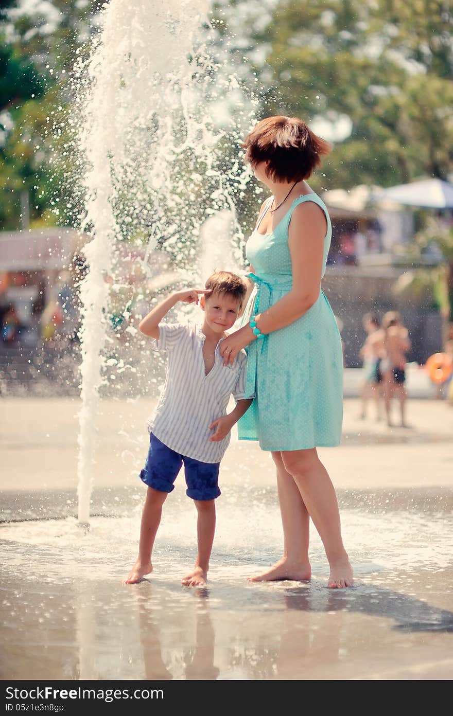 Mother in a turquoise dress with a young son playing at the fountain. Mother in a turquoise dress with a young son playing at the fountain