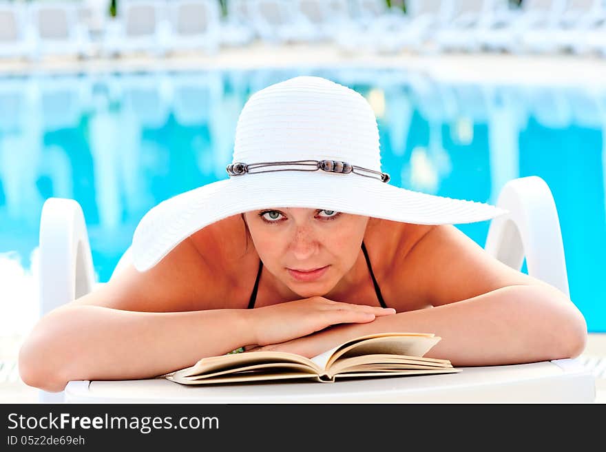 Beautiful girl look in a white hat on a sun lounger beside the pool