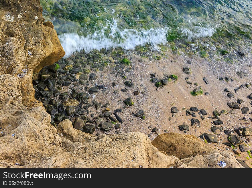 Wave Rolls Onto The Rocks Of Sandy Coast