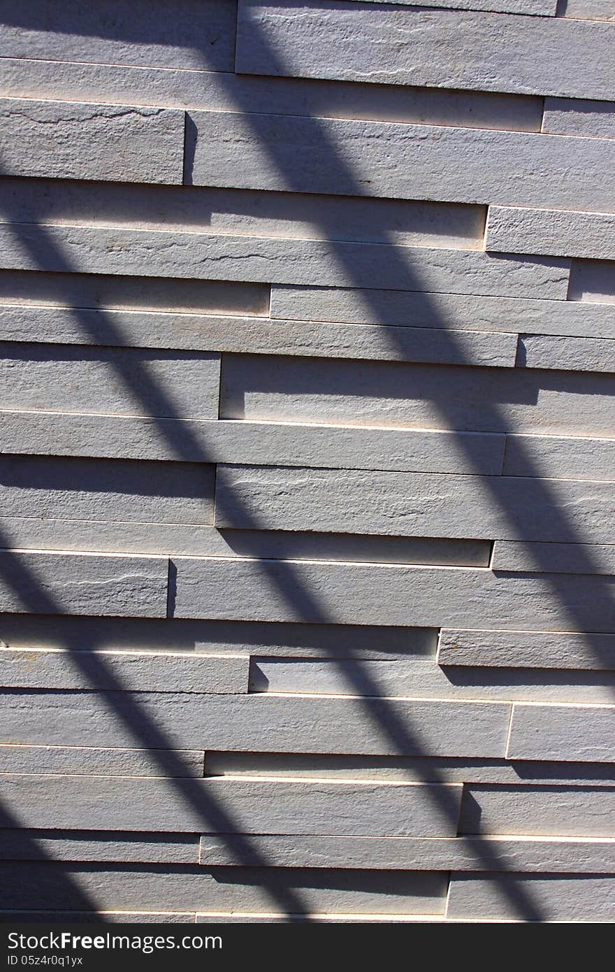 Textured wall made of white bricks and diagonal shadows.