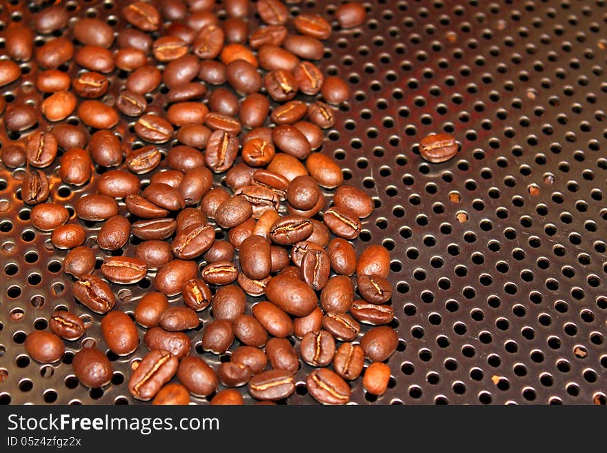 Roasted coffee beans on stainless steel background with holes for ventilation