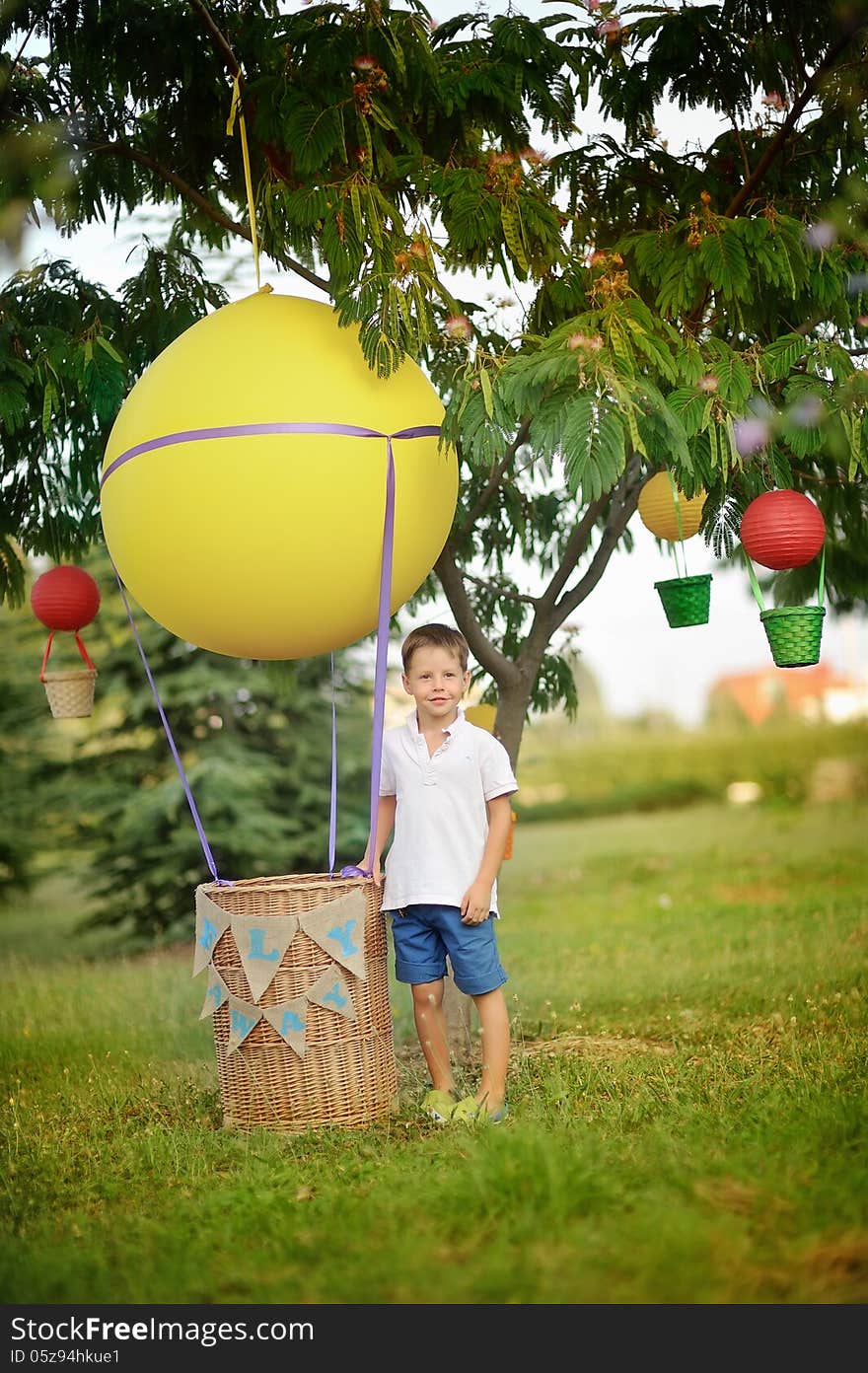 On the green grass boy stands near a hot air balloon with a basket