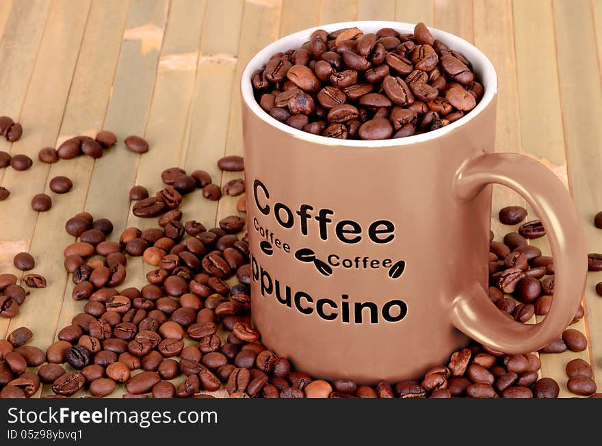 Brown cup with coffee beans is on a wooden table. coffee beans are scattered around the cup. Inscription on the cup coffee, cappuccino. wood background.