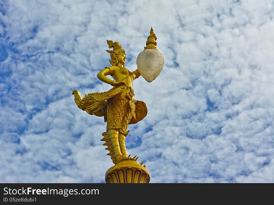 Gold kinnaree statue with lantern and cloudy sky