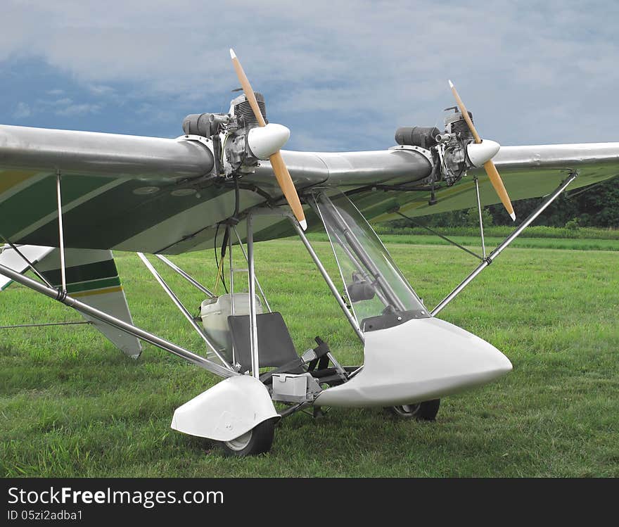 Close-up of a twin engine open cockpit ultralight aircraft sitting on the ground in a field of grass. Close-up of a twin engine open cockpit ultralight aircraft sitting on the ground in a field of grass.