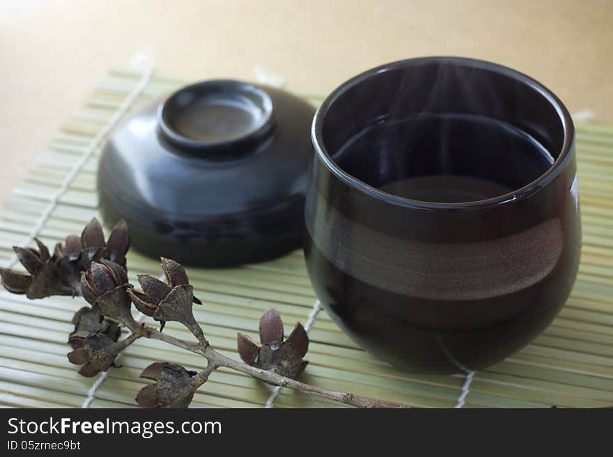 Black cup of tea with steam on brown background