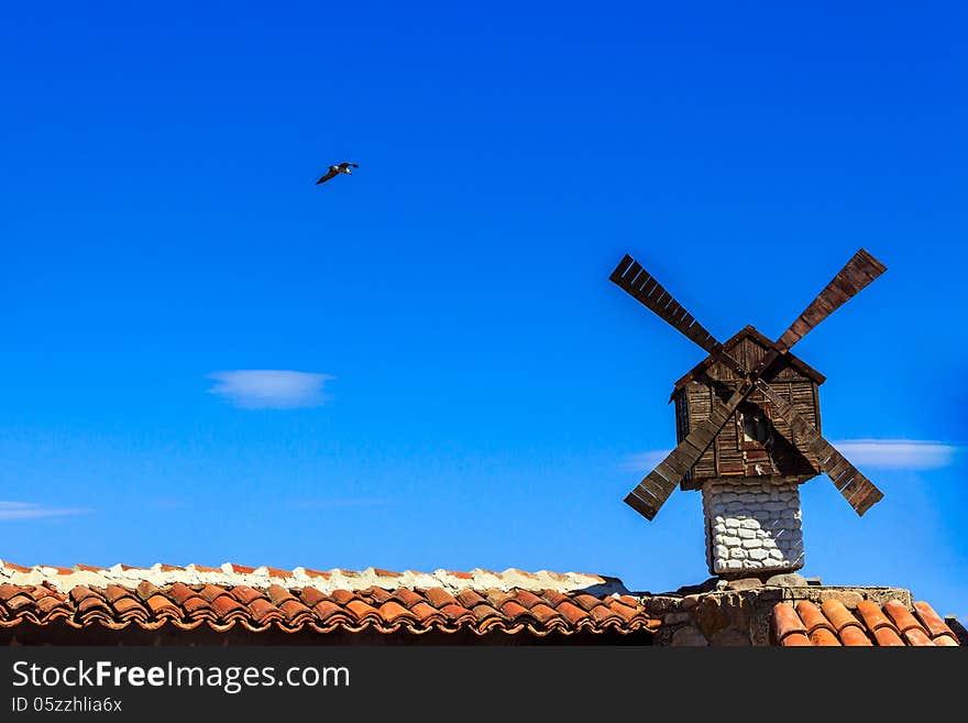 Decorative windmill installed at the Architecture building on a background of the clear sky with a flying seagull. Decorative windmill installed at the Architecture building on a background of the clear sky with a flying seagull