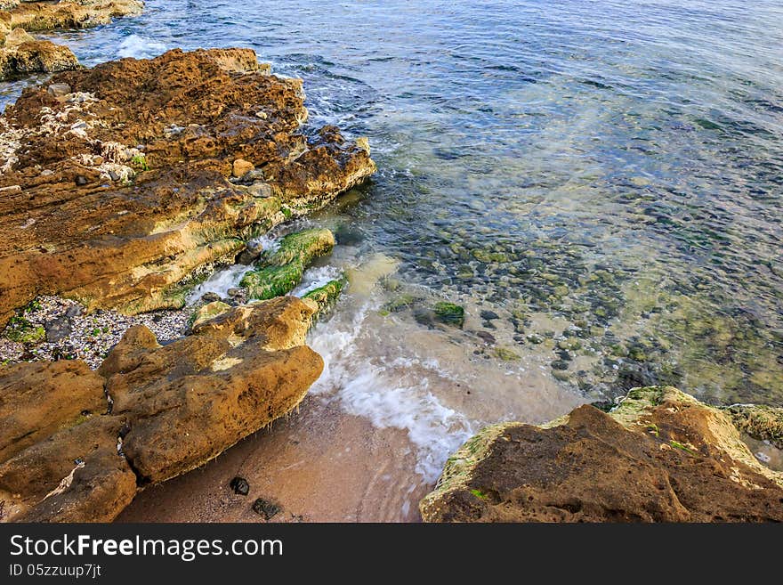 Seabed seen through clear waves crashing stones on shore