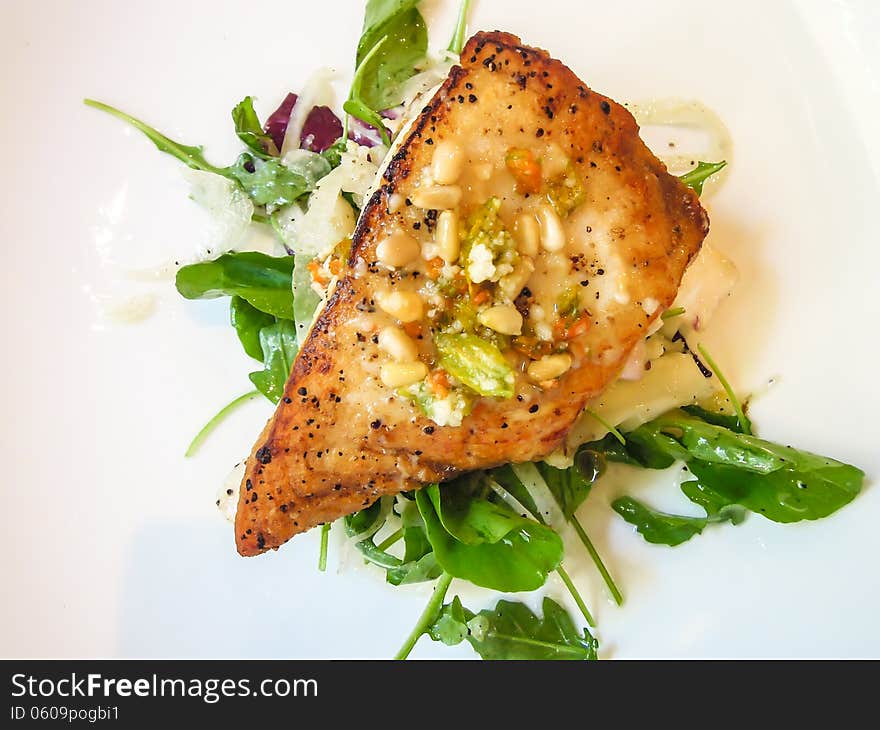 Closeup of fresh pan seared halibut with mixed greens and pine nuts