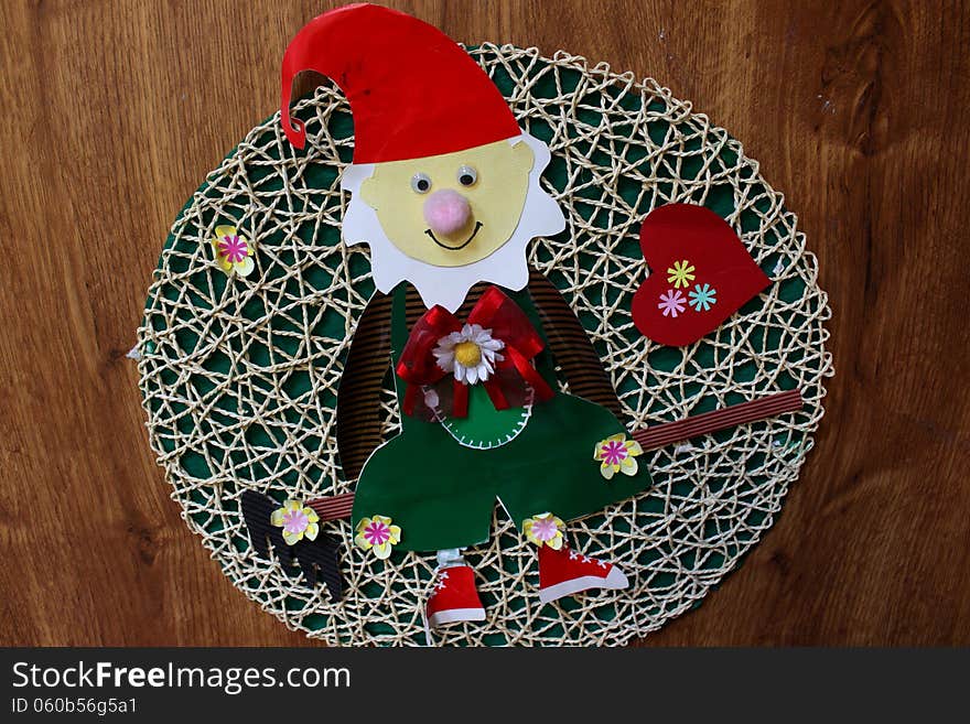 Elf made from colored paper on a braided background placed on wooden door