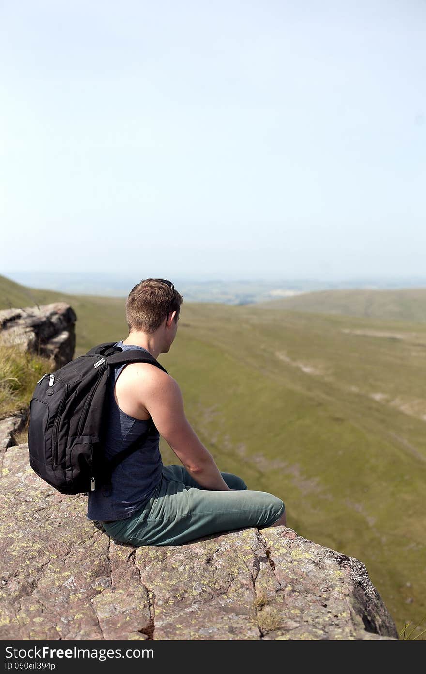 Young man sitting on the rop of the high cliff in mountains, back view. Young man sitting on the rop of the high cliff in mountains, back view