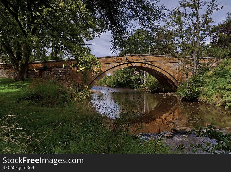 View of the River Esk running under the stone bridge at Lealholm. The River Esk is used for angling. Summer scene Overhanging trees water running over rocks. Sun and shade. View of the River Esk running under the stone bridge at Lealholm. The River Esk is used for angling. Summer scene Overhanging trees water running over rocks. Sun and shade.