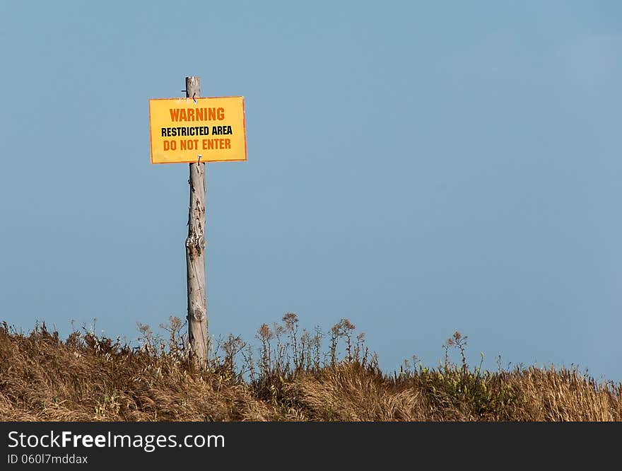 Forbidden territory - a warning sign saying the danger. Yellow sign on the pole at the blue sky background - Warning, Restricted area, Do not enter.