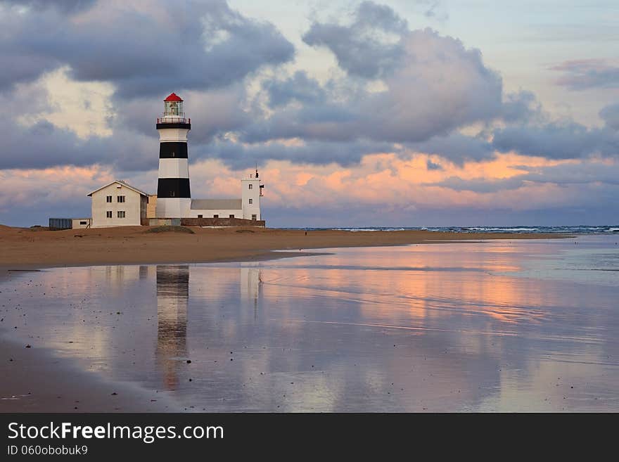 Sunset at beach on South African east coast with lighthouse reflected in sea water. Sunset at beach on South African east coast with lighthouse reflected in sea water