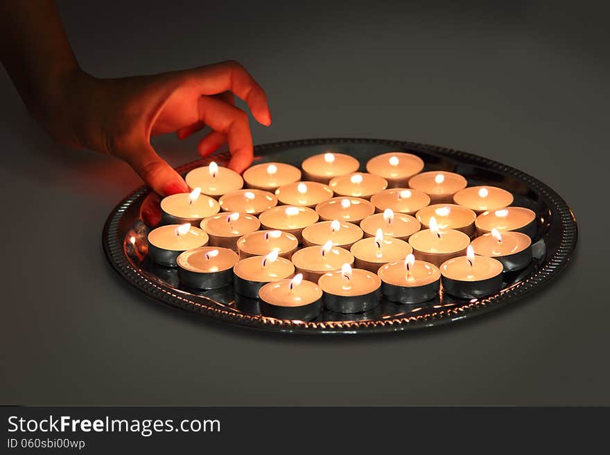 A hand takes candle from a tray with lots of burning candles. A hand takes candle from a tray with lots of burning candles