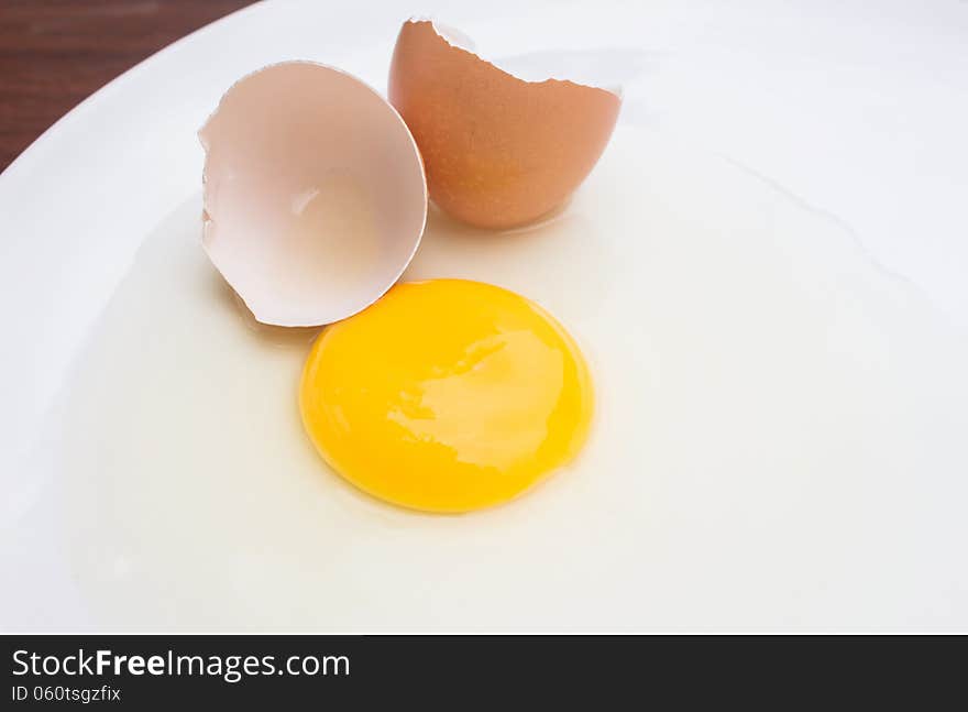 Cracked chicken egg with yolk and egg shell on dish background. Cracked chicken egg with yolk and egg shell on dish background.