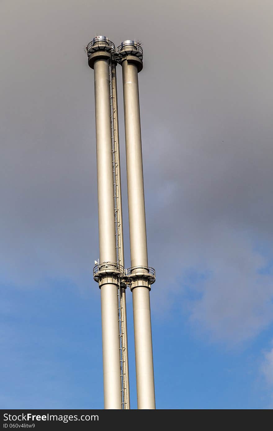 Two metal chimneys against the blue sky with dark clouds