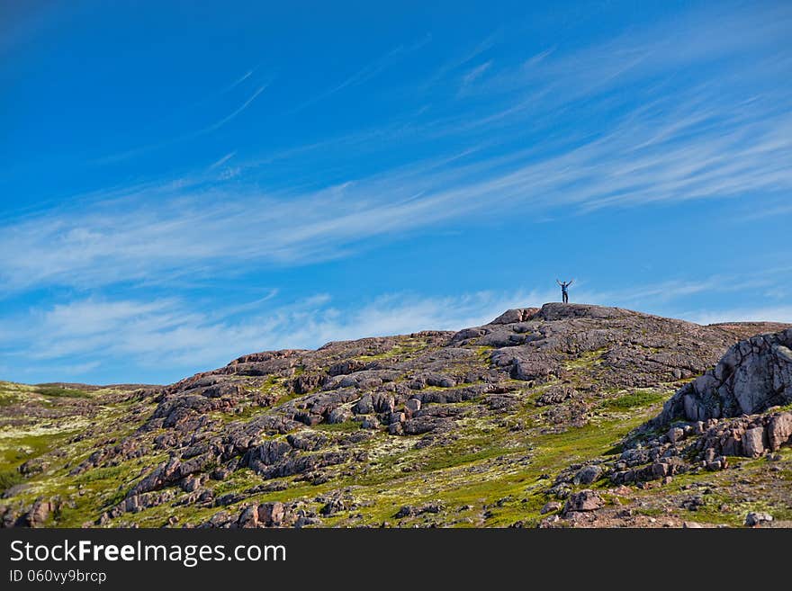 Man with a backpack on a mountain spread wide his hands in the summer against a blue sky with clouds