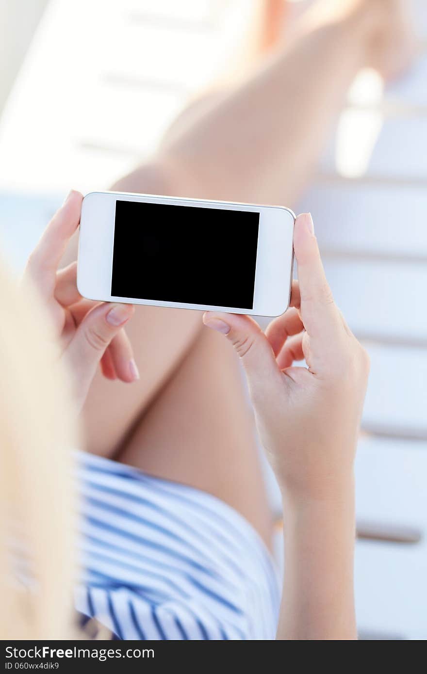 Girl in a bathing suit lying on a white chaise lounge with touch phone