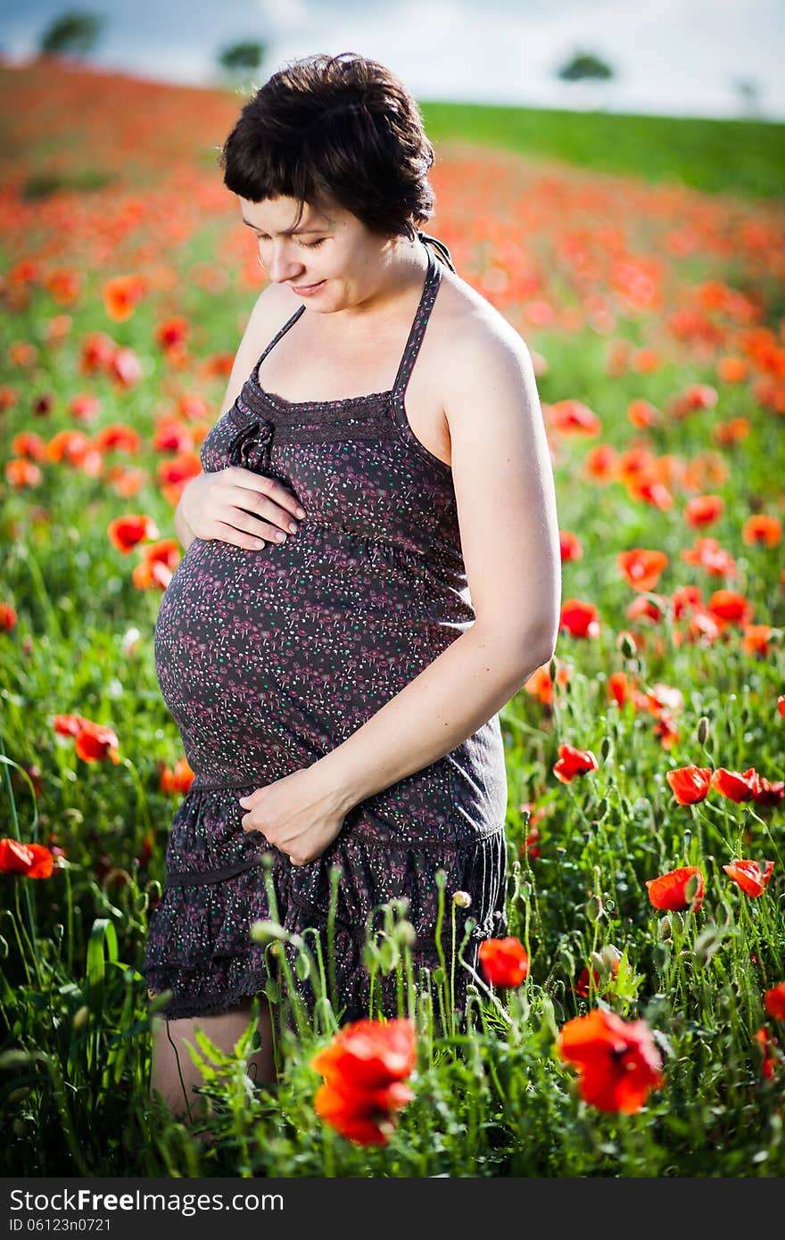 Pregnant happy woman in a flowering poppy field outdoors