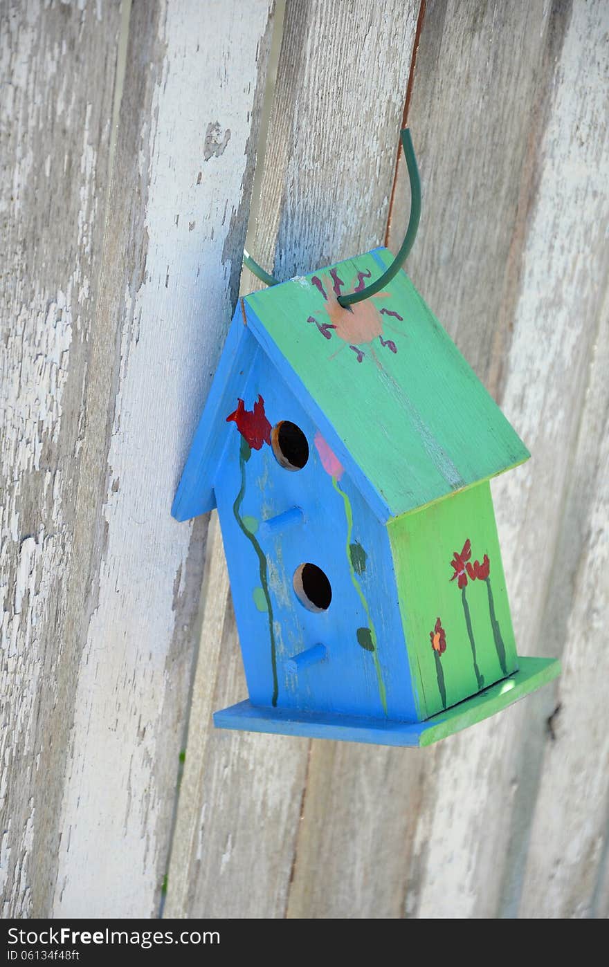 Little blue and green birdhouse hanging on wooden fence