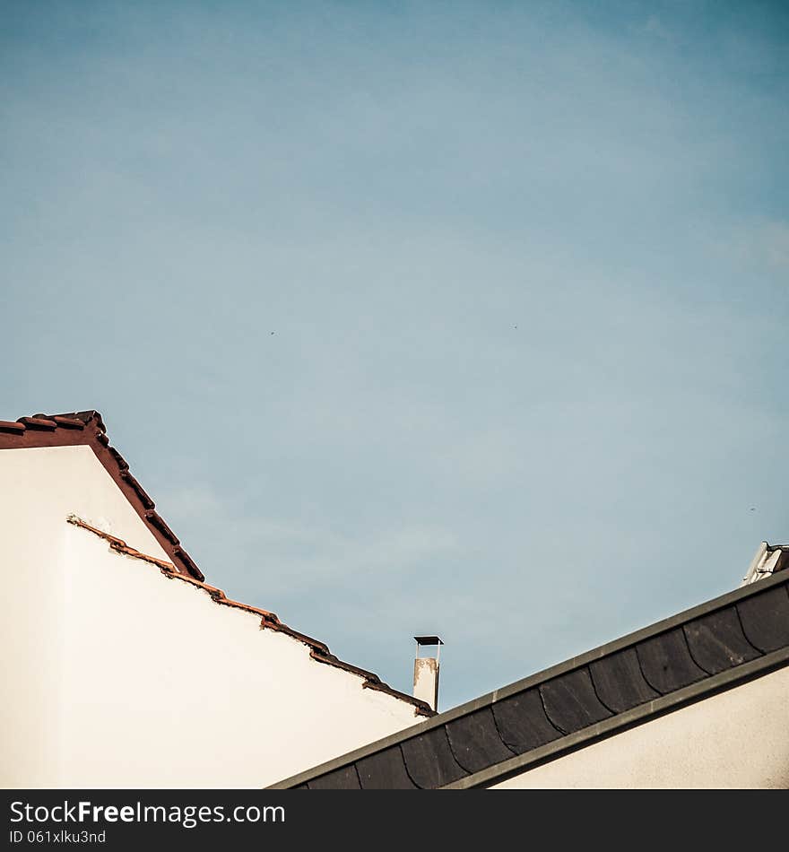 The silhouettes of two roofs crossing in front of a blue sky