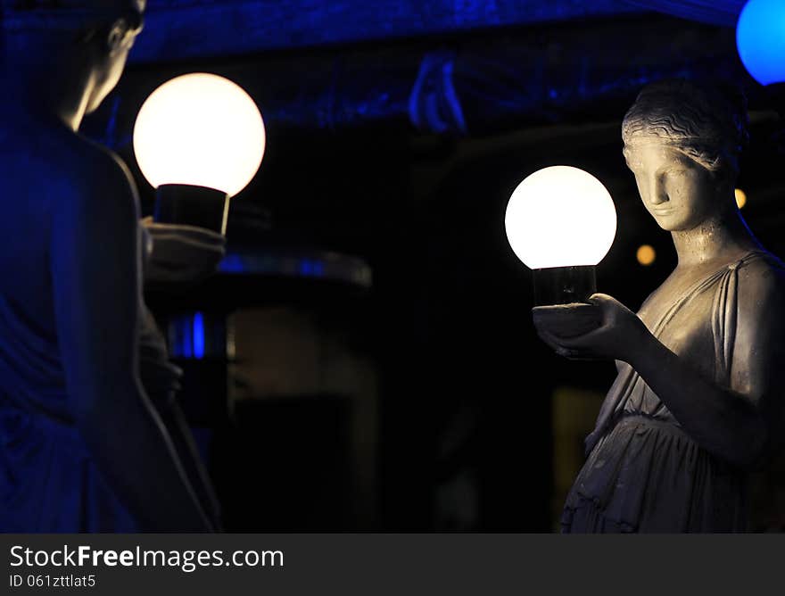 A night time image of two Italian sculptured stone statues of Roman women in traditional, historical roman clothing holding round lighted globes of bright light in their hands. These statues are on the footpath in a busy street in Brisbane city, Queensland, Australia. A night time image of two Italian sculptured stone statues of Roman women in traditional, historical roman clothing holding round lighted globes of bright light in their hands. These statues are on the footpath in a busy street in Brisbane city, Queensland, Australia.