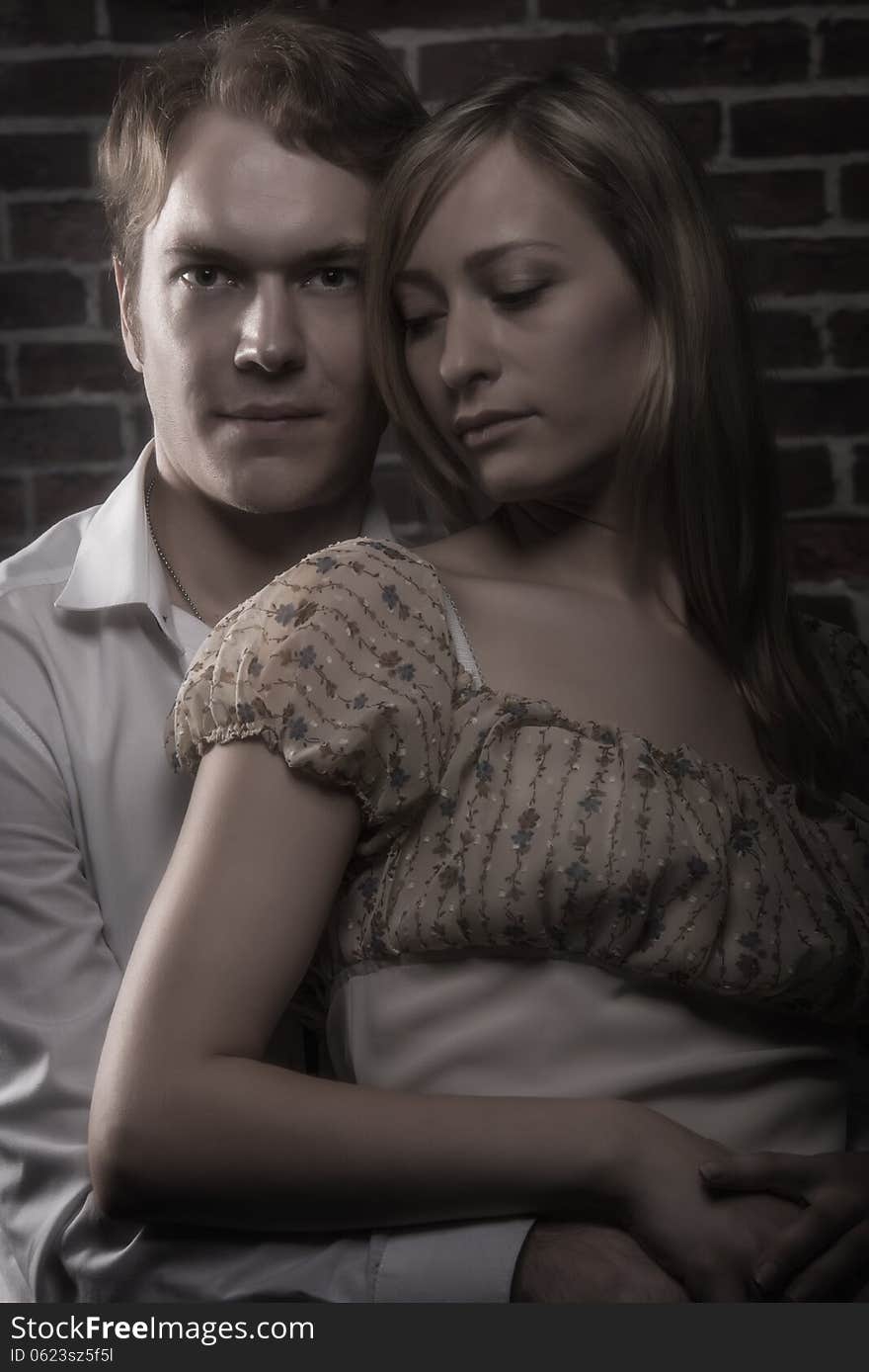 Portrait of couple hugging, posing at studio over red brick wall background. Portrait of couple hugging, posing at studio over red brick wall background.