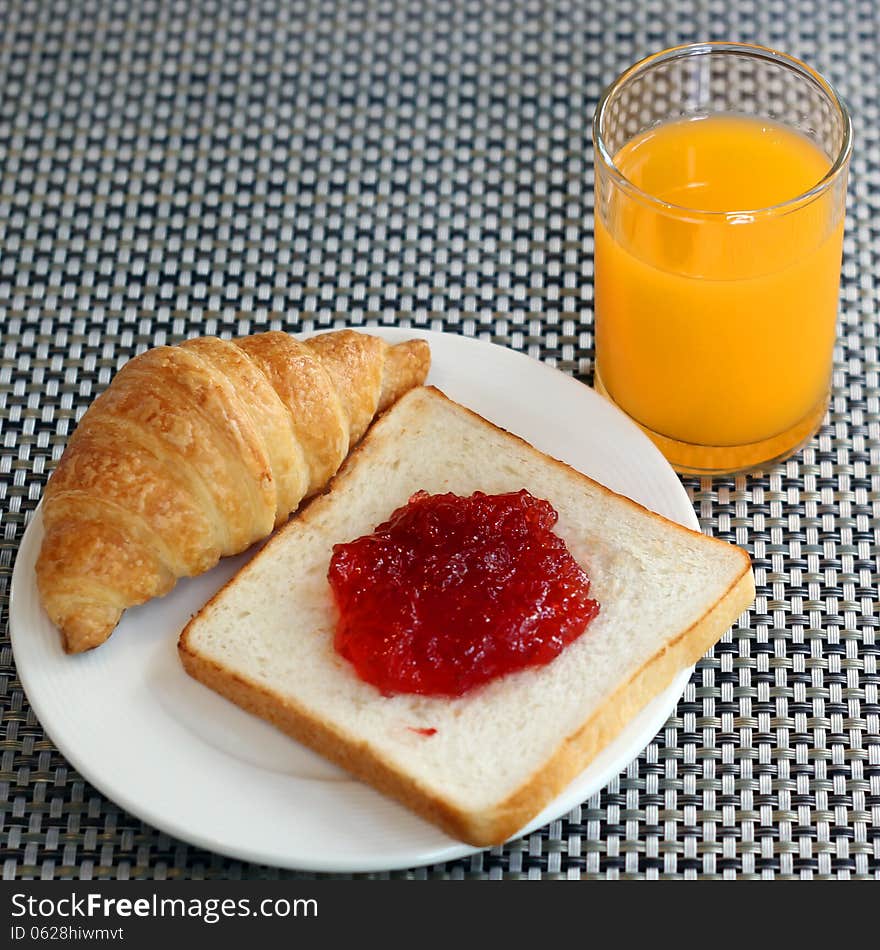 Strawberry jam on bread, croissant  and orange juice