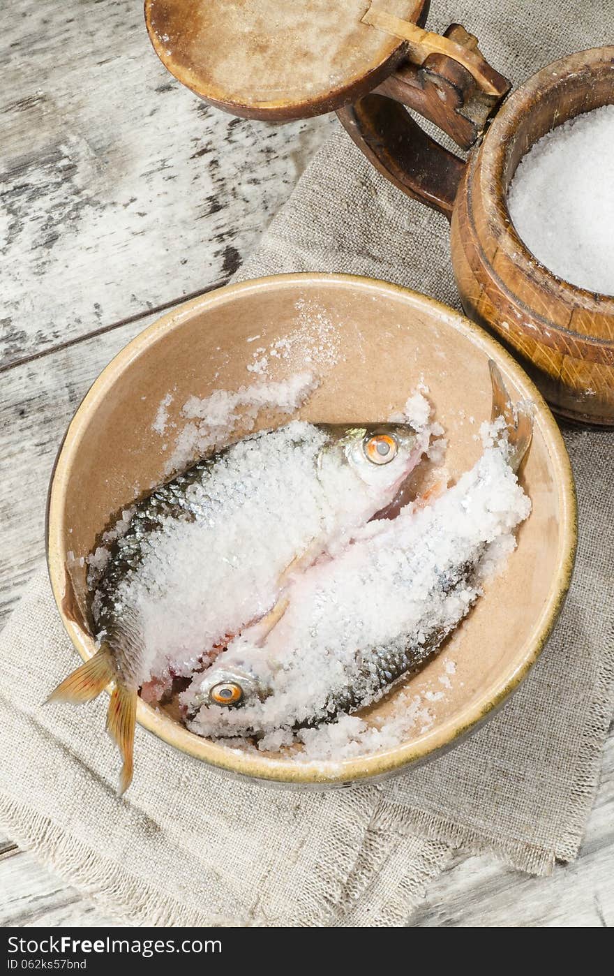 Two roaches fish in ceramic bowl with salt., near the old cutlery. From the series Still Life with fresh fish