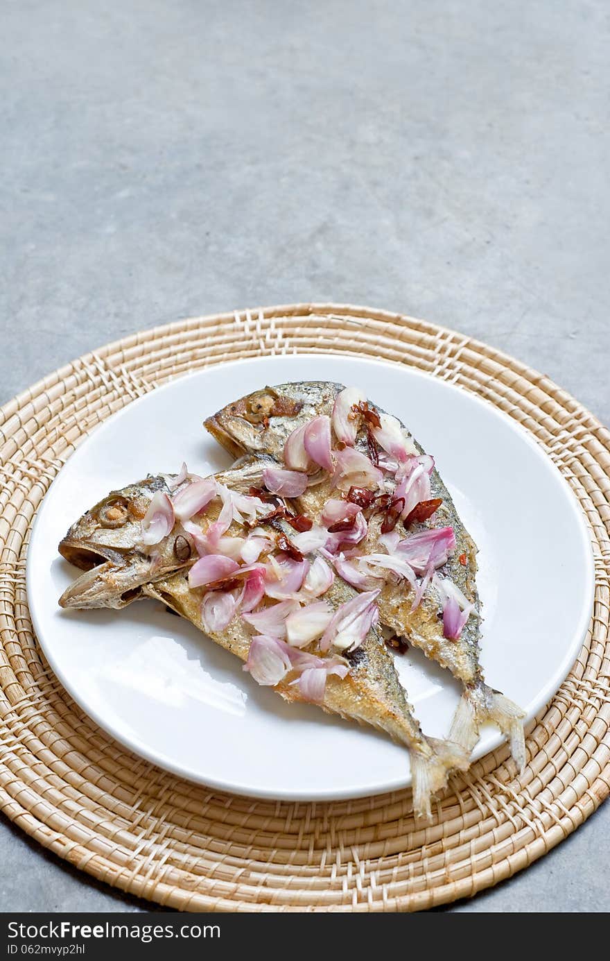 Deep fry two mackerrel fish topping with sliced shallot and chilli on white plate. Deep fry two mackerrel fish topping with sliced shallot and chilli on white plate