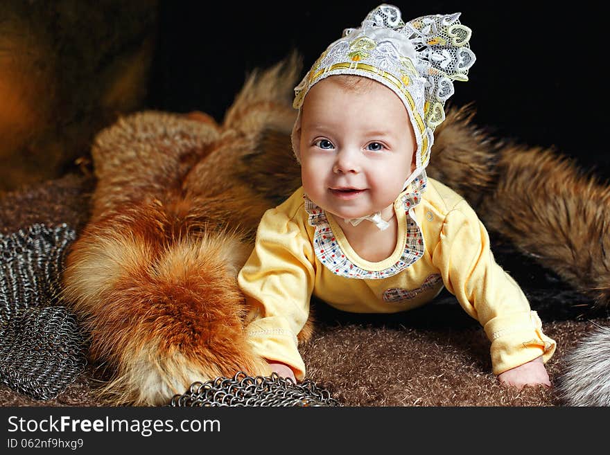 Blue-eyed baby lying on fur litter near the hauberk, fox pelt in the background. Blue-eyed baby lying on fur litter near the hauberk, fox pelt in the background