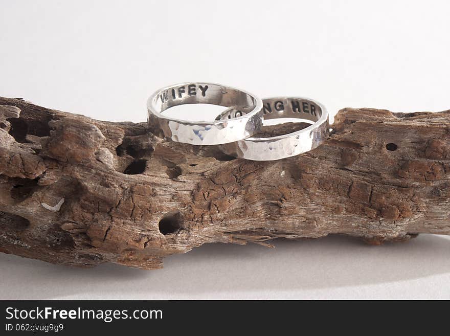 Two hammered sterling silver engagement rings on a piece of driftwood. Two hammered sterling silver engagement rings on a piece of driftwood
