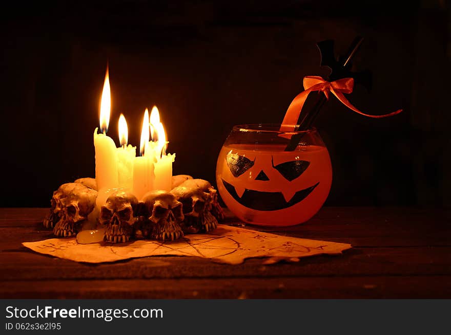 Orange Halloween drink with evil candles on wooden table in the darkness