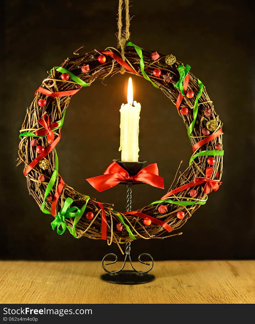 Christmas wreath with burning candle and red bow on wooden table and black background. Christmas wreath with burning candle and red bow on wooden table and black background