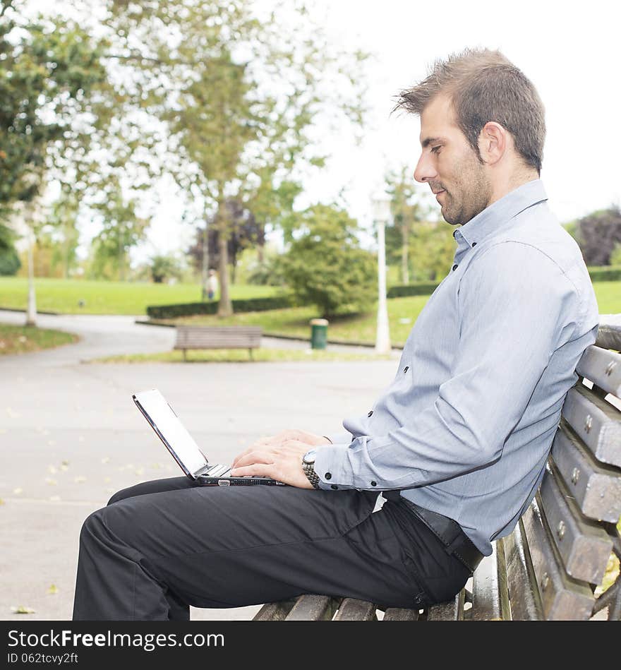 Man sitting in the wooden bench and working with computer.