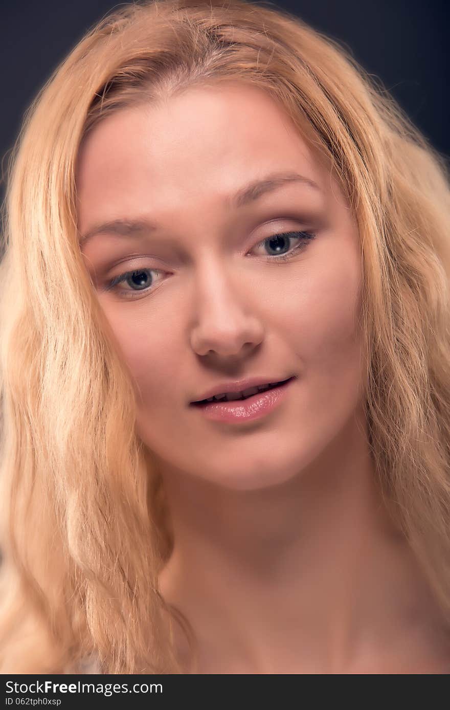 Close up portrait of natural looking young woman with healthy facial skin, long golden blond hair, big beautiful eyes. Over dark blue background. Close up portrait of natural looking young woman with healthy facial skin, long golden blond hair, big beautiful eyes. Over dark blue background.