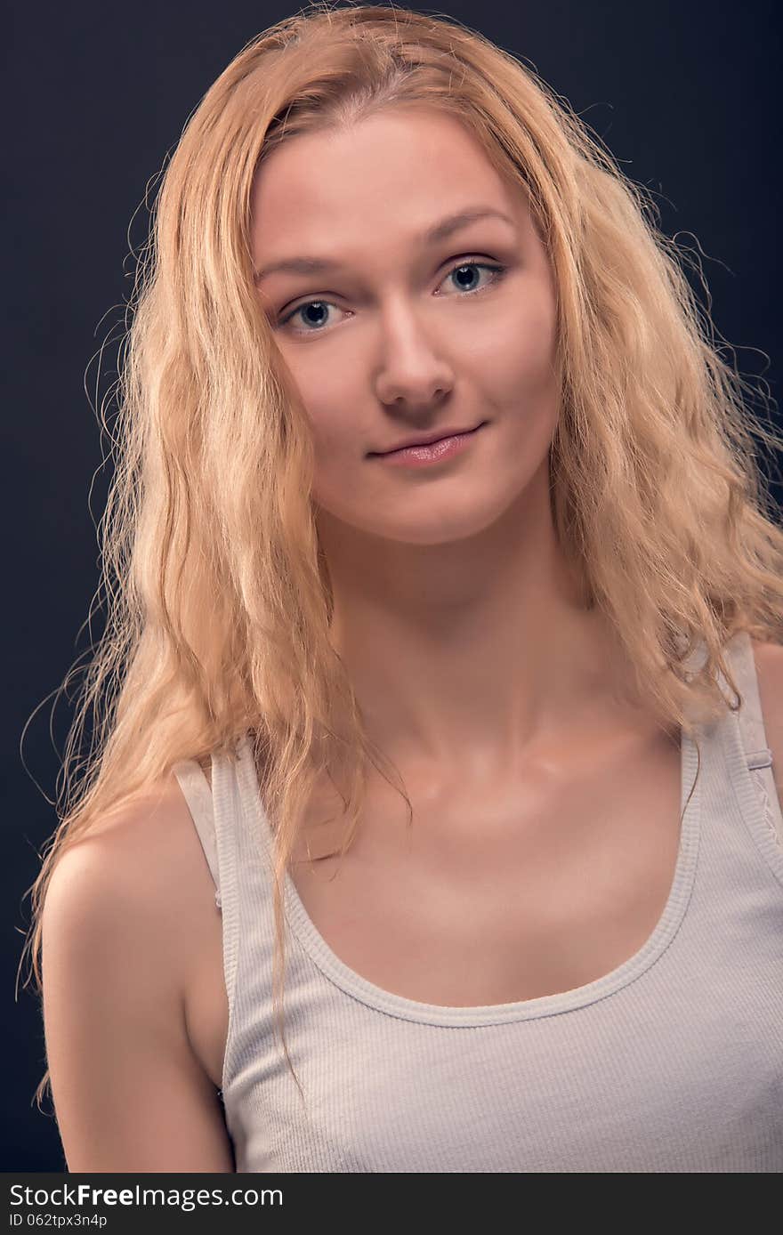 Portrait of natural looking young woman with healthy facial skin, long golden blond hair, big beautiful eyes and lovely smile. Over dark blue background. Portrait of natural looking young woman with healthy facial skin, long golden blond hair, big beautiful eyes and lovely smile. Over dark blue background.