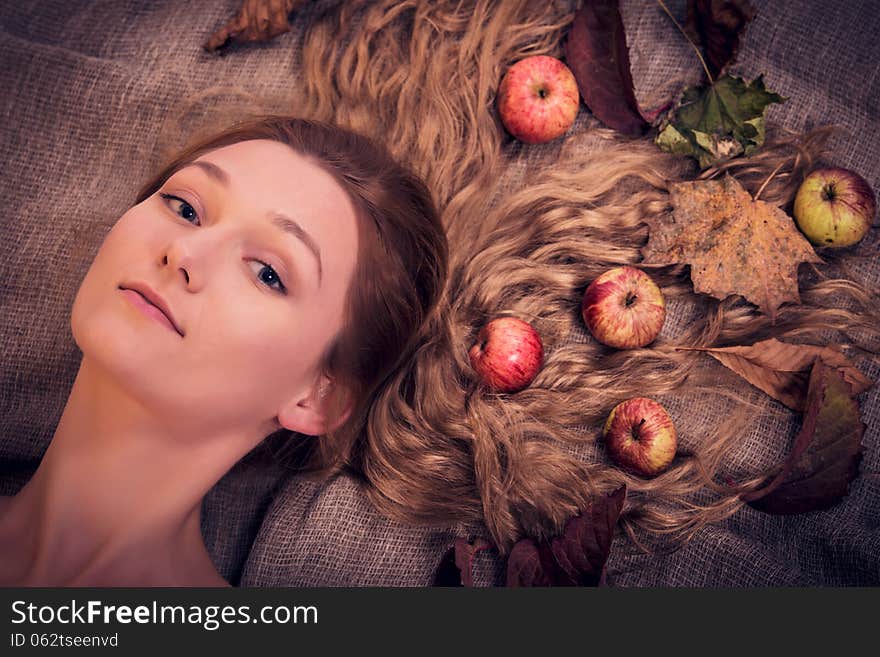 Portrait of beautiful girl with autumn leaves and apples in her gorgeous golden hair, lying over canvas material, looking dreamily at You. Portrait of beautiful girl with autumn leaves and apples in her gorgeous golden hair, lying over canvas material, looking dreamily at You.