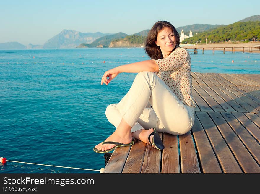 Girl Sitting On A Pier Near The Sea