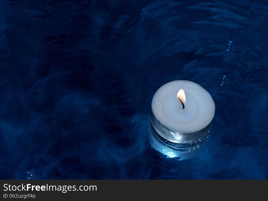 White burning candle on water with a few bubbles