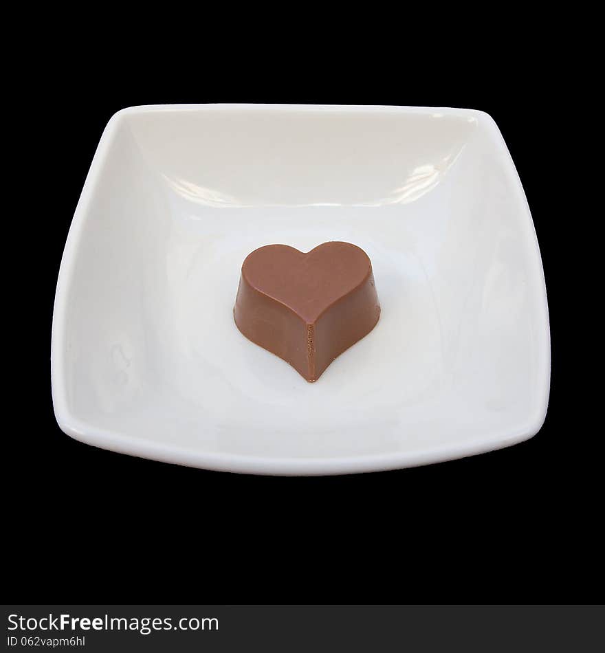 Studio isolated chocolate heart in a white plate over black background