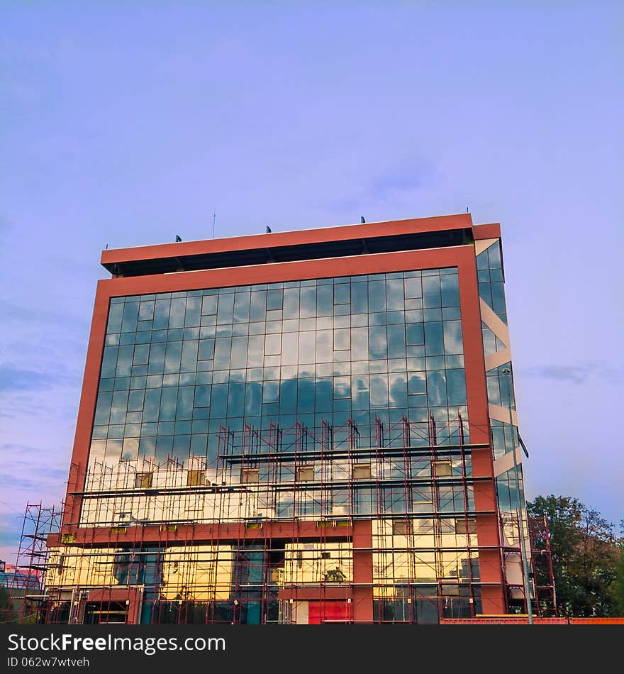 Modern glass building under construction with mounted scaffolds reflecting sunset. Modern glass building under construction with mounted scaffolds reflecting sunset