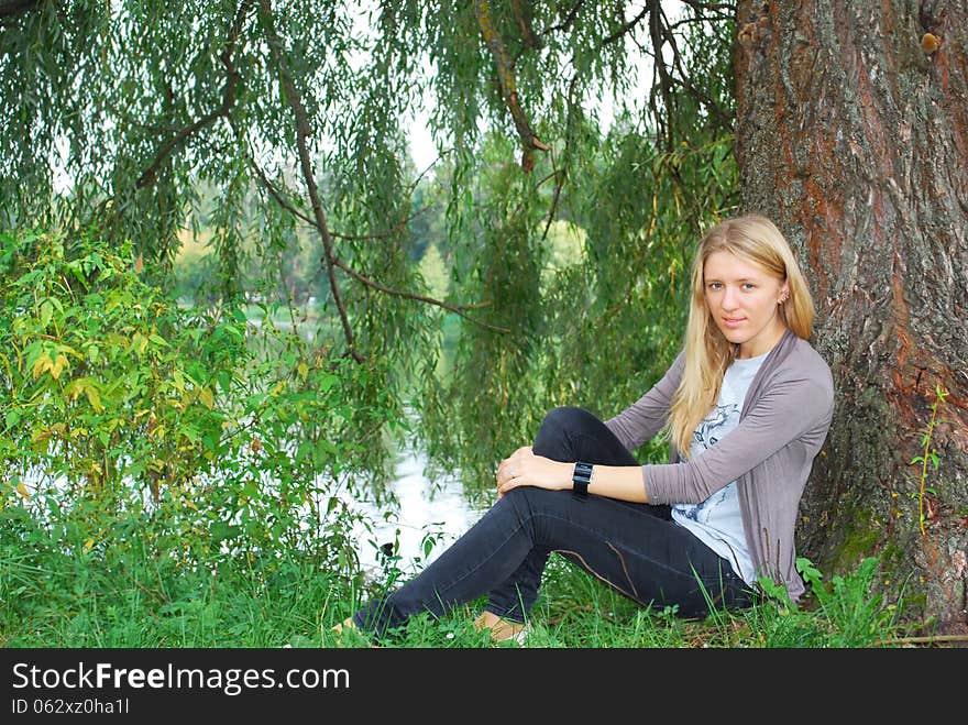 The girl sitting near willow near the lake.