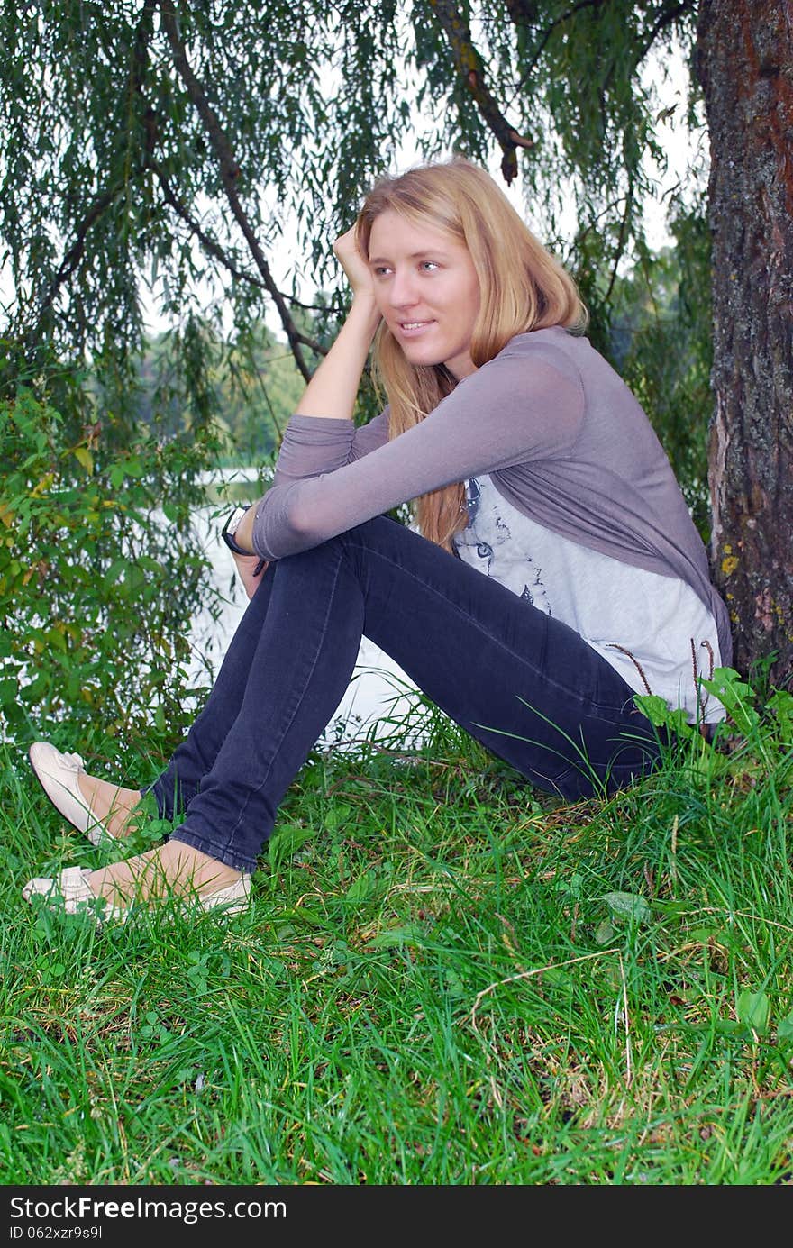 In the summer, the girl sitting near willow near the lake.