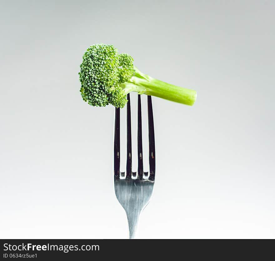 Broccoli on a fork over a gray white background