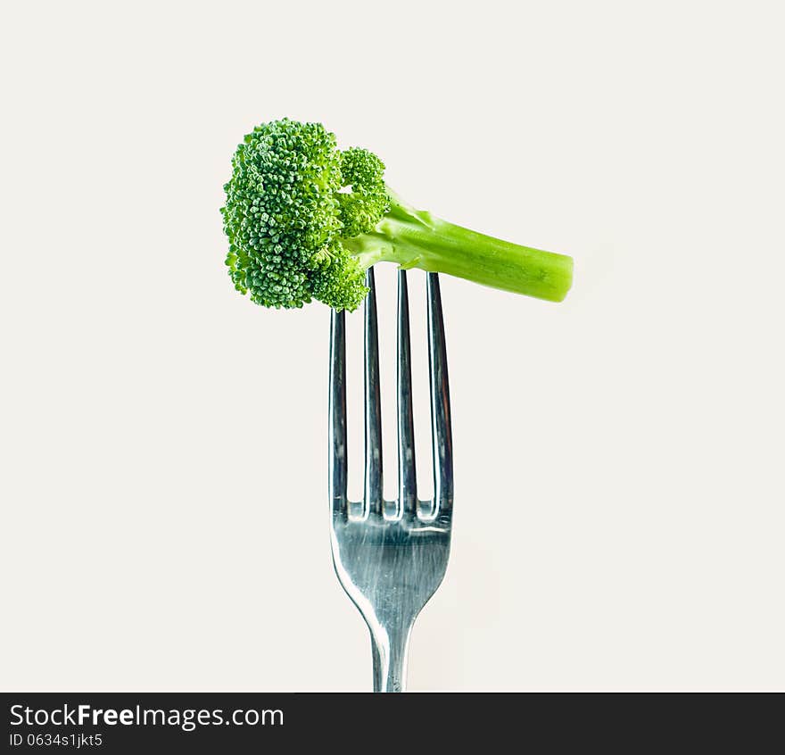 Broccoli on a fork over a warm gray white background