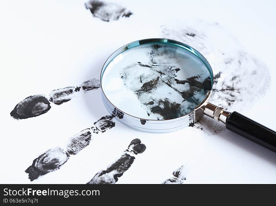 Crime concept. Black fingerprints and magnifying glass on white background