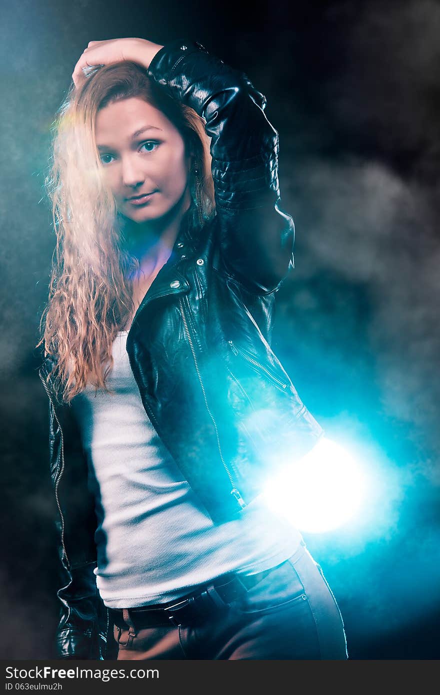 Portrait of amazing young woman with curly blond hair dressed in stylish black jacket. Over blue color spotlight. Portrait of amazing young woman with curly blond hair dressed in stylish black jacket. Over blue color spotlight.