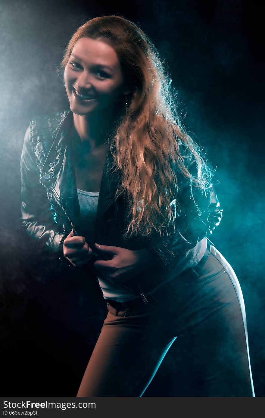 Portrait of amazing young woman with curly blond hair dressed in stylish black jacket. Over blue color spotlight. Portrait of amazing young woman with curly blond hair dressed in stylish black jacket. Over blue color spotlight.